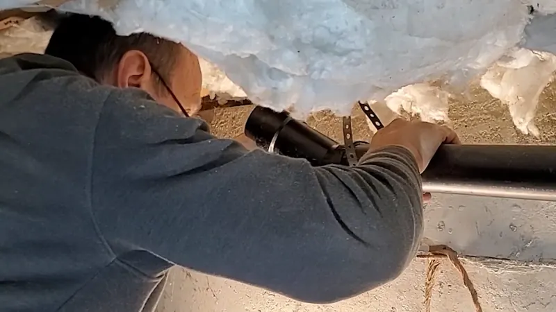 Close view of crawlspace drain pipe repair below a home for plumbing service in Enola